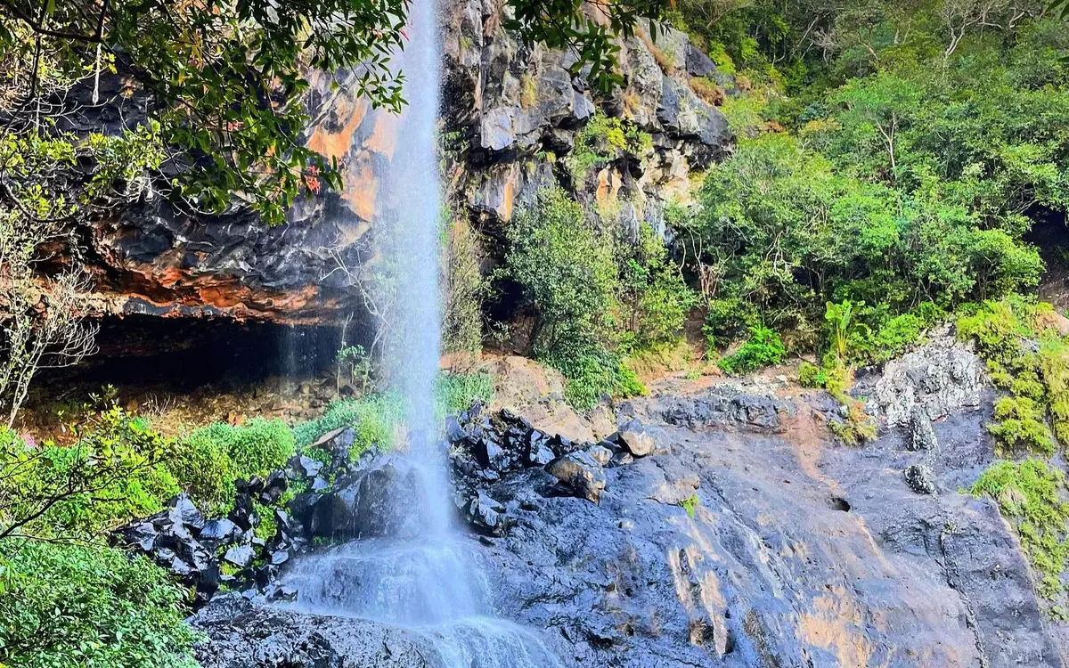 Un seul jet d'eau tombant sur des blocs de roche volcanique noire, un faible arc-en-ciel dans les embruns