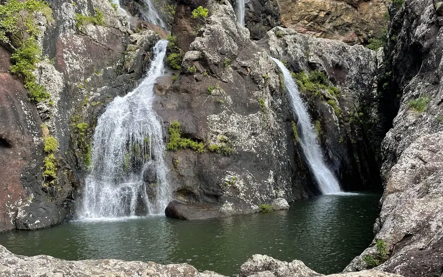 Deux cascades tombant le long d&rsquo;une paroi rocheuse grise dans un bassin vert sombre entouré de blocs