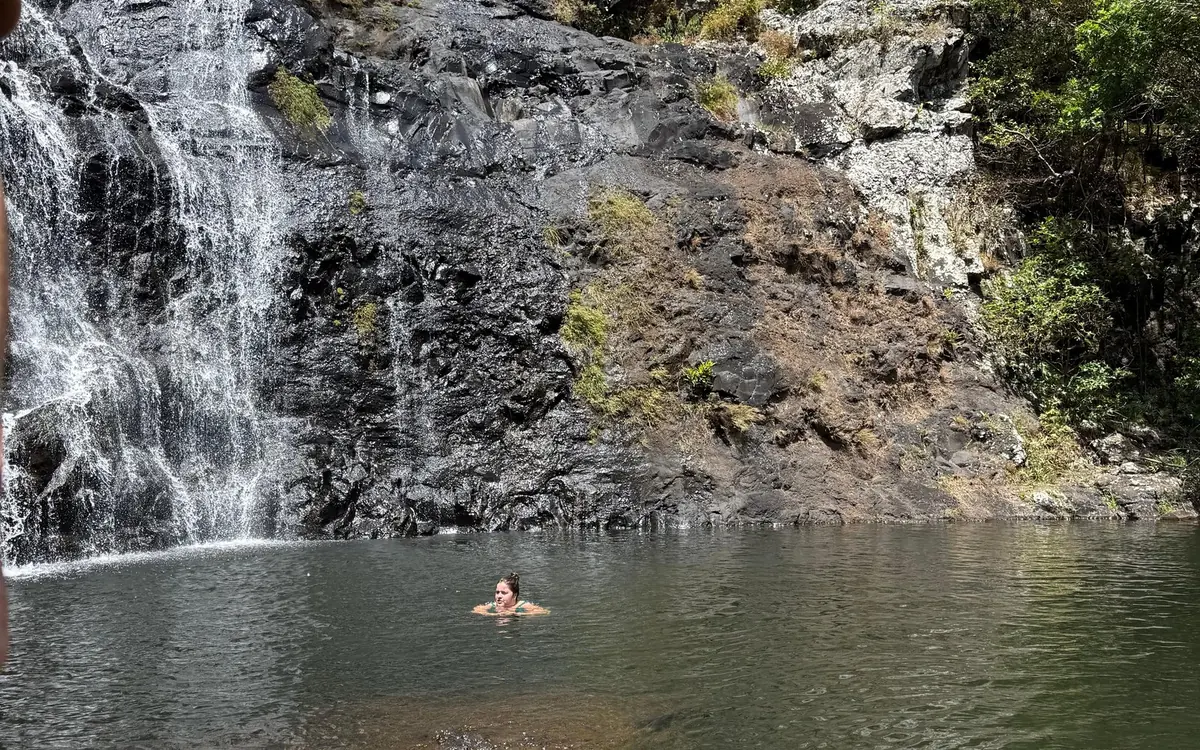 Un nageur dans un bassin sombre sous un large rideau d'eau sur la roche noire