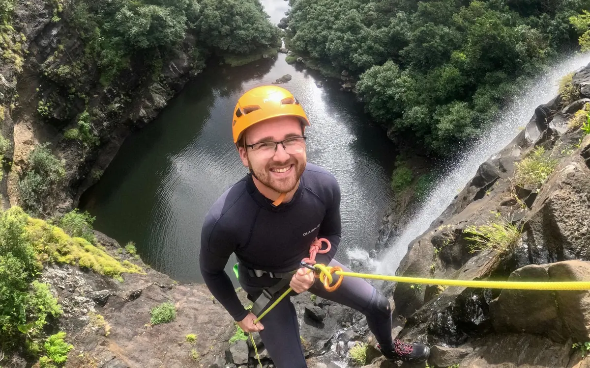 Une personne en combinaison et casque orange tenant une corde au bord d&rsquo;une falaise